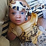 baby, infant, headband, blue_eyes, mittens, yellow_clothing, tutu, striped_pillow, couch, face, person, cute, indoor, portrait, child, young, sitting, fabric, pattern, soft