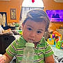 baby_bottle, child, couch, curly_hair, cute, face, furniture, green_shirt, home, indoor, living_room, milk, natural_light, person, portrait, striped_clothing, toddler, toys, window, young_child
