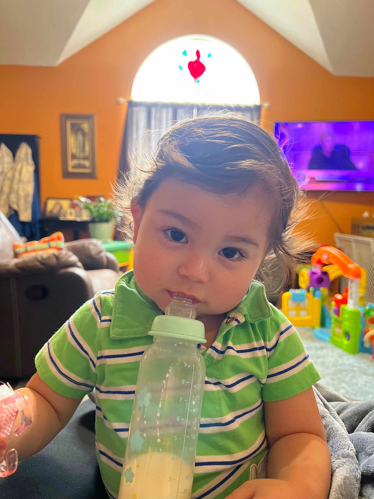 Kosei joined the competition — help win amazing prizes! baby_bottle, child, couch, curly_hair, cute, face, furniture, green_shirt, home, indoor, living_room, milk, natural_light, person, portrait, striped_clothing, toddler, toys, window, young_child