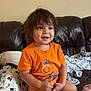 blanket, casual, child, couch, cozy, cute, face, furniture, hair, happy, home, indoors, orange_tshirt, person, playful, relaxed, seated, smiling, toddler, young_child
