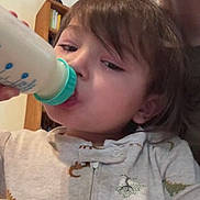 Kosei joined the competition — help win amazing prizes! child, toddler, baby_bottle, drinking, onesie, dinosaur_print, indoor, bookshelf, wooden_furniture, face, hair, person, clothing, close_up, infant, cute, young_child, casual, cozy, portrait