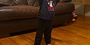 Kosei is registered to the contest to win money with this photo: toddler, child, barefoot, standing, arms_up, smiling, indoor, wooden_floor, leather_couch, toy, desk, clothing, happy, person, home, furniture, young_child, dark_clothes, living_room, expression