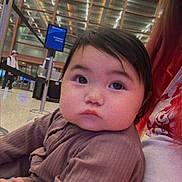 Aera joined the competition — help win amazing prizes! baby, child, infant, person, indoor, airport, terminal, seated, curious, face, cute, clothing, adult_arm, tattoo, modern_ceiling, information_sign, waiting_area, public_space, young_child, portrait