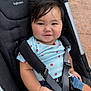 baby, child, smile, stroller, seatbelt, clothing, denim_shorts, blue_shirt, strawberry_pattern, face, hand, hair, outdoor, pavement, cute, happy, infant, safety_harness, person, closeup