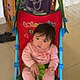child, baby, indoor, stroller, toy, smiling, curious, pink_clothing, purple_shirt, floor_tile, kitchen, cabinet, wheel, play, sibling, happy, person, young_child, infant, family