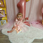 Liséa participe au concours pour gagner de l'argent avec cette photo : baby, girl, pink_dress, headband, balloon, number_one, birthday, celebration, fluffy_rug, wooden_floor, golden_crown, blocks, letters, curtains, fairy_lights, smiling, sitting, indoor, decorations, first_birthday
