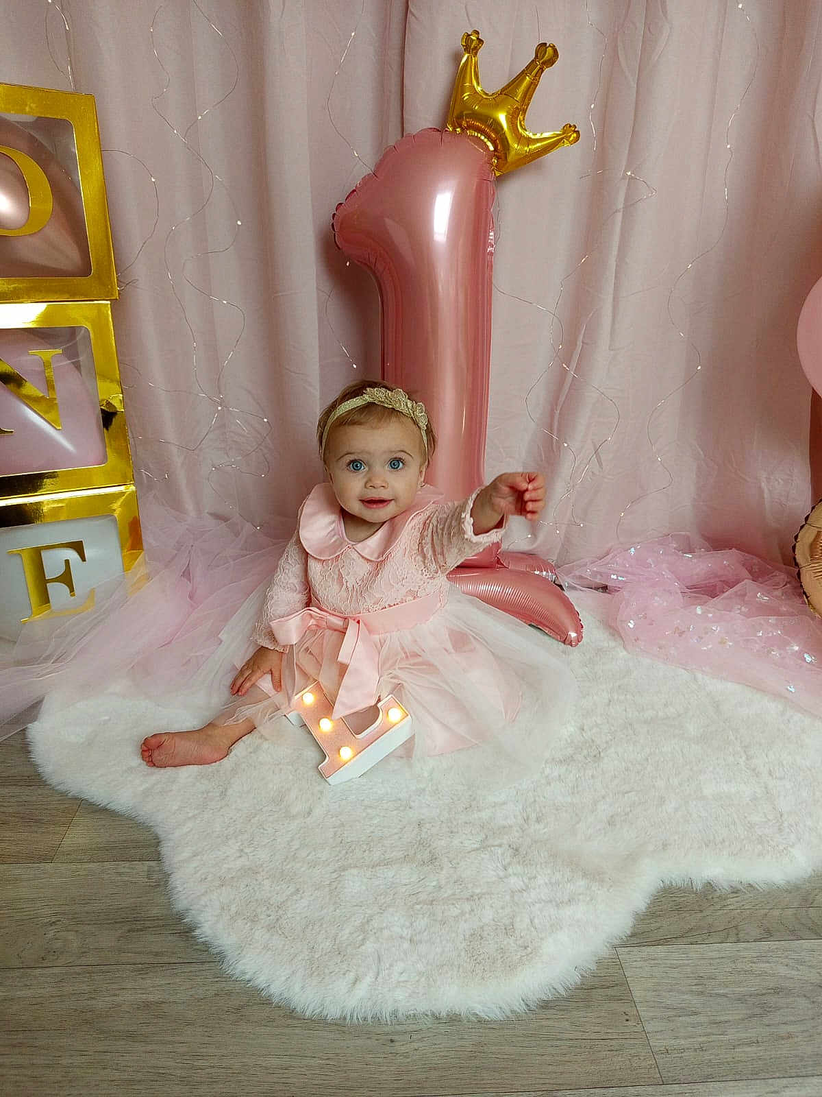 Liséa participe au concours pour gagner de l'argent avec cette photo : baby, girl, pink_dress, headband, balloon, number_one, birthday, celebration, fluffy_rug, wooden_floor, golden_crown, blocks, letters, curtains, fairy_lights, smiling, sitting, indoor, decorations, first_birthday