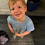 child, boy, smile, blonde_hair, blue_shirt, standing, indoor, floor, happy, portrait, person, casual_clothing, young, looking_up, light_shadow, wooden_floor, cute, toddler, skin, hair