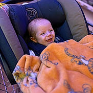 Rowan joined the competition — help win amazing prizes! baby, car_seat, blanket, orange, tiger_print, shopping_cart, smiling, child, indoor, happy, clothing, person, cute, infant, seat, fabric, cozy, head, face, comfort