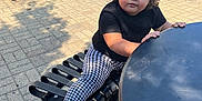 Logann joined the competition — help win amazing prizes! bench, black_shirt, building, car, casual_clothing, child, curious_expression, curly_hair, daytime, houndstooth_leggings, outdoor, person, shadow, sidewalk, sneakers, street, sunny, table, toddler, window
