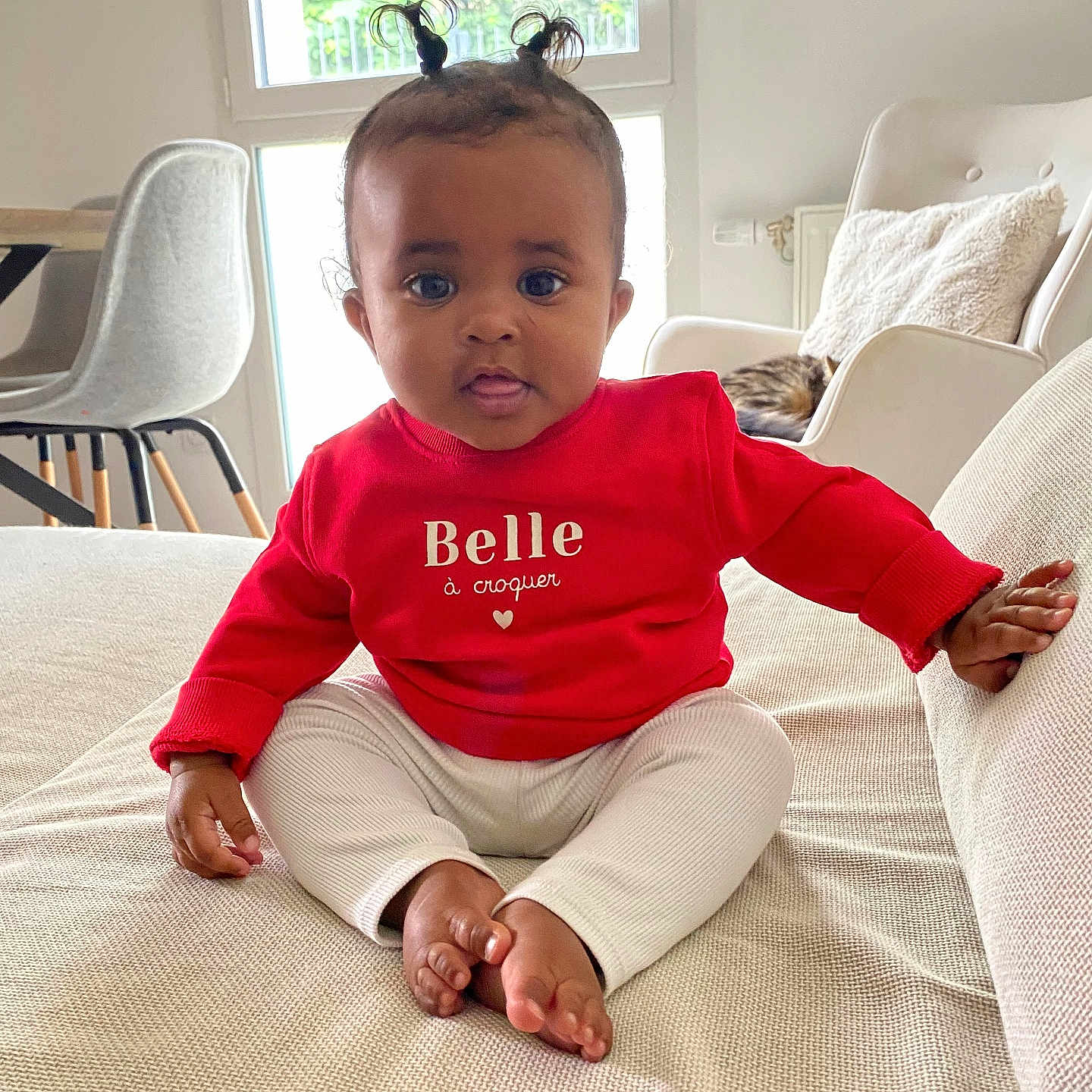 Haneya a rejoint le concours — aidez-le/la à gagner de superbes lots ! baby, chair, child, couch, cute, floor, furniture, home, indoor, living_room, natural_light, person, pillow, pony_tail, portrait, red_sweater, sitting, table, white_pants, window