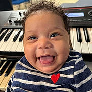 Dreyona is registered to the contest to win money with this photo: baby, child, smiling, tongue_out, curly_hair, striped_shirt, red_heart, keyboard, musical_instrument, indoor, happy, cute, portrait, face, blue, white, person, infant, expression, closeup