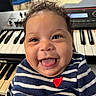 baby, child, smiling, tongue_out, curly_hair, striped_shirt, red_heart, keyboard, musical_instrument, indoor, happy, cute, portrait, face, blue, white, person, infant, expression, closeup