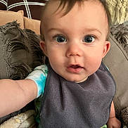 Thayer is registered to the contest to win money with this photo: baby, infant, child, portrait, close_up, wide_eyes, sitting, bib, couch, pillows, blanket, home, indoors, face, eyes, brown_hair, clothing, cozy, selfie, photography