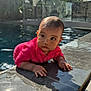 baby, baby_clothing, child, curious, daylight, face, glass_fence, greenery, hands, outdoor, person, pink_sweater, pool, reflection, shadow, sunlight, swimming_pool, tile, water, wet
