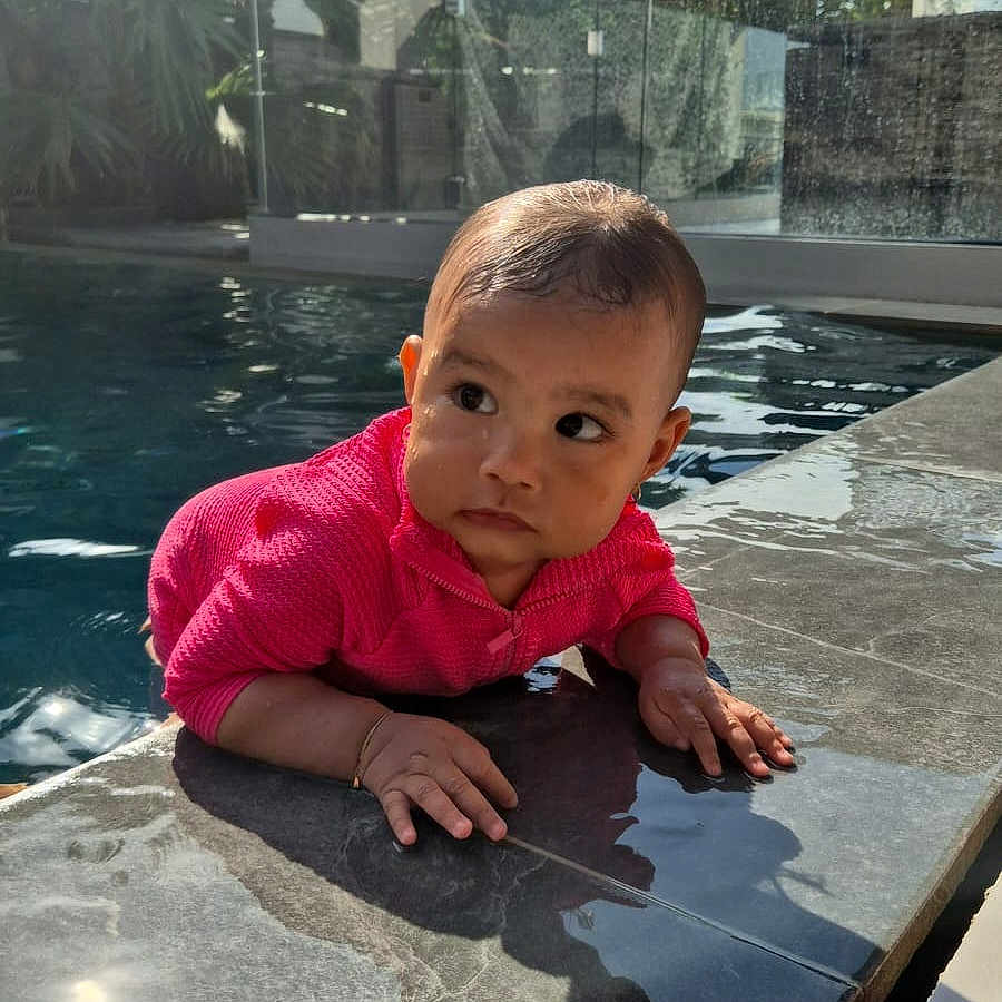 Nellya a rejoint le concours — aidez-le/la à gagner de superbes lots ! baby, baby_clothing, child, curious, daylight, face, glass_fence, greenery, hands, outdoor, person, pink_sweater, pool, reflection, shadow, sunlight, swimming_pool, tile, water, wet