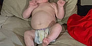 Oliver is registered to the contest to win money with this photo: baby, diaper, couch, beige, infant, hand, face, living_room, plant, digital_clock, pillow, red_cloth, skin, expression, furniture, person, indoors, casual, cute, relaxing