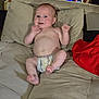 baby, diaper, couch, beige, infant, hand, face, living_room, plant, digital_clock, pillow, red_cloth, skin, expression, furniture, person, indoors, casual, cute, relaxing