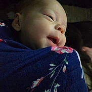Paizleigh is registered to the contest to win money with this photo: baby, infant, child, face, portrait, sleepy, smiling, side_eye, close_up, blanket, floral_pattern, blue, clothing, indoors, cozy, soft_lighting, low_light, seated, head, photography