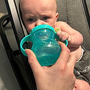 Mason joined the competition — help win amazing prizes! baby, infant, child, sippy_cup, cup, hand, adult_hand, feeding, seat, stroller, gray_fabric, closeup, portrait, furrowed_brow, eyes, skin, arm, clothing, person, expression