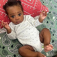 Keyran participe au concours pour gagner de l'argent avec cette photo : baby, infant, onesie, patterned_blanket, paisley, pillow, curious, lying_down, hands_up, barefoot, indoors, cute, child, person, face, expression, young, skin, clothing, resting