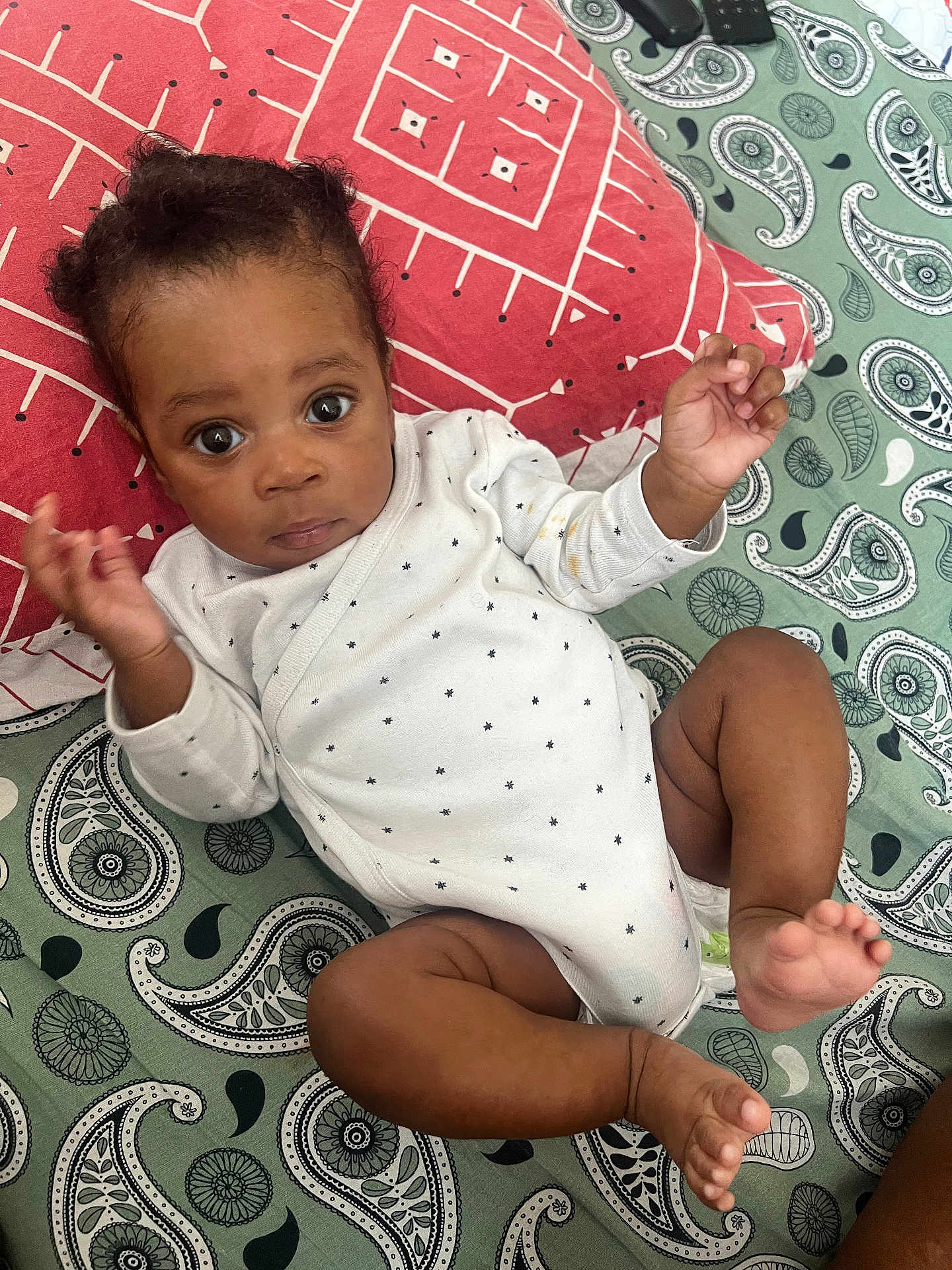 Keyran participe au concours pour gagner de l'argent avec cette photo : baby, infant, onesie, patterned_blanket, paisley, pillow, curious, lying_down, hands_up, barefoot, indoors, cute, child, person, face, expression, young, skin, clothing, resting