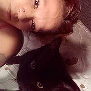 Priscilla is registered to the contest to win money with this photo: animal, black_cat, casual, cat, close_up, companion, face, indoor, intimate, lying_down, mattress, nose_ring, person, pet, portrait, quiet, relaxing, shoulder, tattoo, warm_lighting