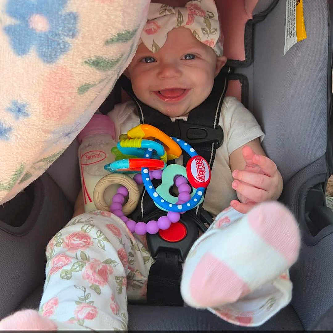 Ainsley joined the competition — help win amazing prizes! baby, car_seat, smiling, toy, blanket, bottle, headband, floral_pattern, pajamas, child, cute, happy, infant, colorful, seatbelt, indoors, portrait, footwear, soft_toy, playtime