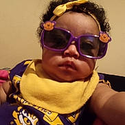 Damiria Wiggins is registered to the contest to win money with this photo: baby, infant, child, portrait, selfie, sunglasses, purple_sunglasses, headband, yellow_bow, scarf, curly_hair, serious_expression, sitting, indoor, couch, clothing, fashion, closeup, face, person
