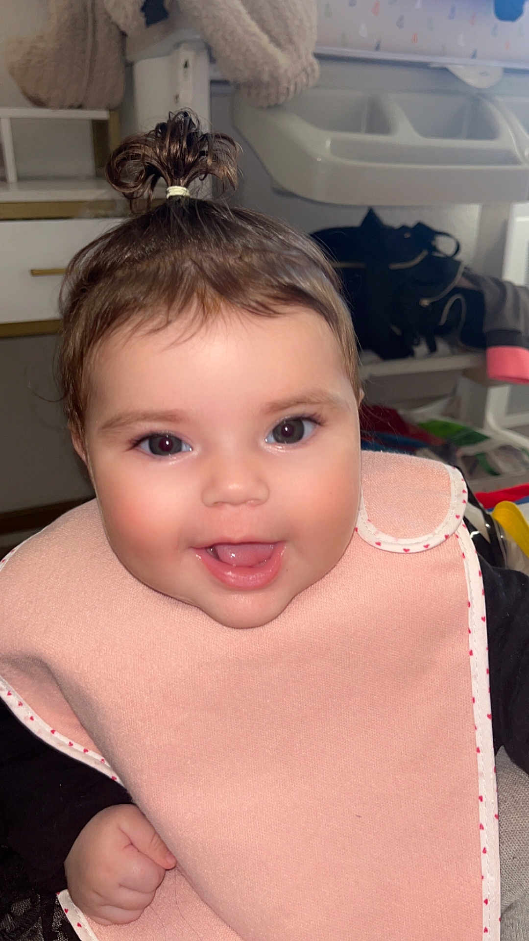 Ayline a rejoint le concours — aidez-le/la à gagner de superbes lots ! baby, smiling, child, indoors, bib, pink, hair_tie, cute, face, happy, person, portrait, infant, hand, clothing, young_child, room, sitting, expression, closeup