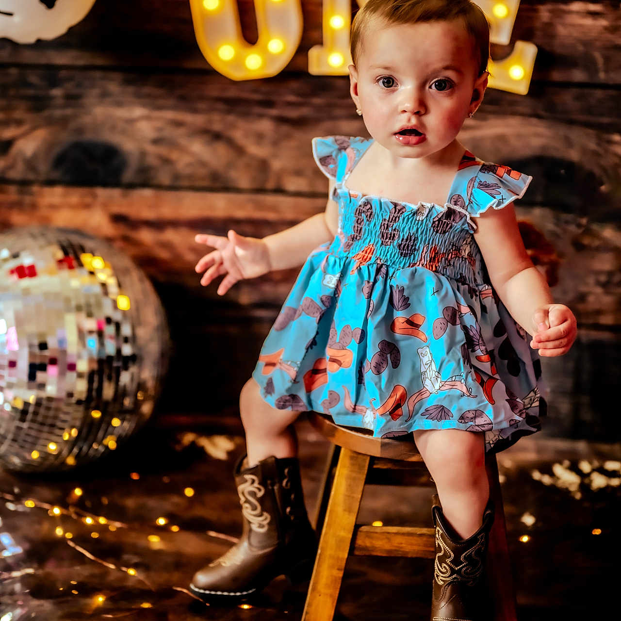 Hadlee is registered to the contest to win money with this photo: balloons, birthday, celebration, child, cowboy_boots, cute, disco_ball, dress, first_birthday, girl, happy, indoor, lighting, one_year_old, party, portrait, stool, string_lights, toddler, wooden_background