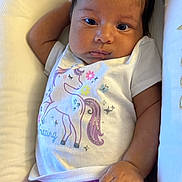 Nova is registered to the contest to win money with this photo: baby, infant, child, unicorn, white_shirt, pink_pants, cushion, seat, relaxed, cute, portrait, indoors, clothing, hand, face, skin, hair, smile, comfort, resting