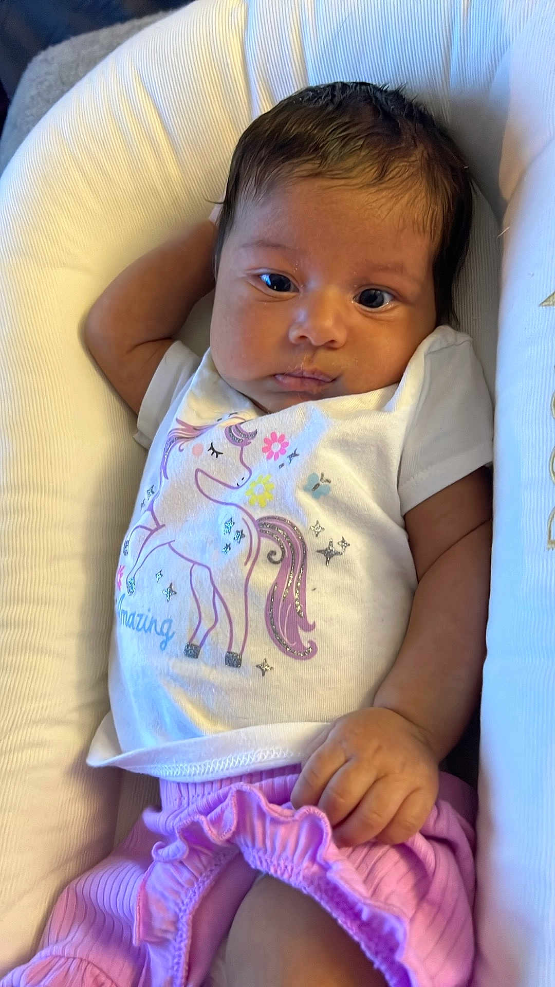 Nova is registered to the contest to win money with this photo: baby, infant, child, unicorn, white_shirt, pink_pants, cushion, seat, relaxed, cute, portrait, indoors, clothing, hand, face, skin, hair, smile, comfort, resting
