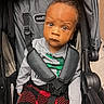 child, toddler, stroller, baby, seatbelt, blanket, red, gray, clothing, indoor, face, person, expression, curious, looking, sitting, head, hair, safety, toy