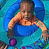 baby, child, inflatable_ring, pool, water, orange_clothing, purple_ball, hand, sunlight, outdoor, playtime, summer, float, aquatic_theme, curious_expression, blue, colorful, fun, toy, swimming