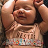 baby, smiling, arms_up, infant, sleeping, shirt, text_on_clothing, strap, rainbow, unicorn, closeup, cozy, indoor, resting, cute, child, peaceful, person, portrait, soft_lighting