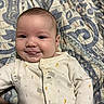 Nalani is registered to the contest to win money with this photo: baby, smiling, tongue_out, onesie, quilt, patterned_blanket, infant, cute, face, child, lying_down, indoors, portrait, cheeks, sleepwear, expression, human, soft_lighting, closeup, happy
