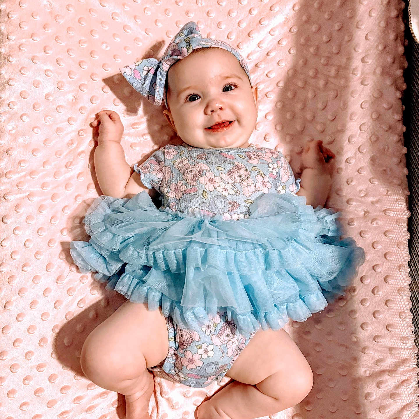 Nalani joined the competition — help win amazing prizes! baby, infant, smile, blue_tutu, headband, floral_onesie, pink_blanket, chubby_legs, cute, happy, lying_down, baby_clothes, child, portrait, indoor, soft_texture, hands_up, bright_eyes, adorable, playful