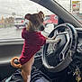 dog, puppy, hoodie, car_interior, steering_wheel, rain, window, raindrops, keys, person, seat, dashboard, side_mirror, red_clothing, brown_dog, white_paws, curious, pet, vehicle, indoor