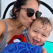 Benjamin is registered to the contest to win money with this photo: woman, toddler, child, sunglasses, kiss, smile, happy, towel, striped_clothing, outdoor, tent, affection, hair, skin, face, person, summer, vacation, closeup, playful