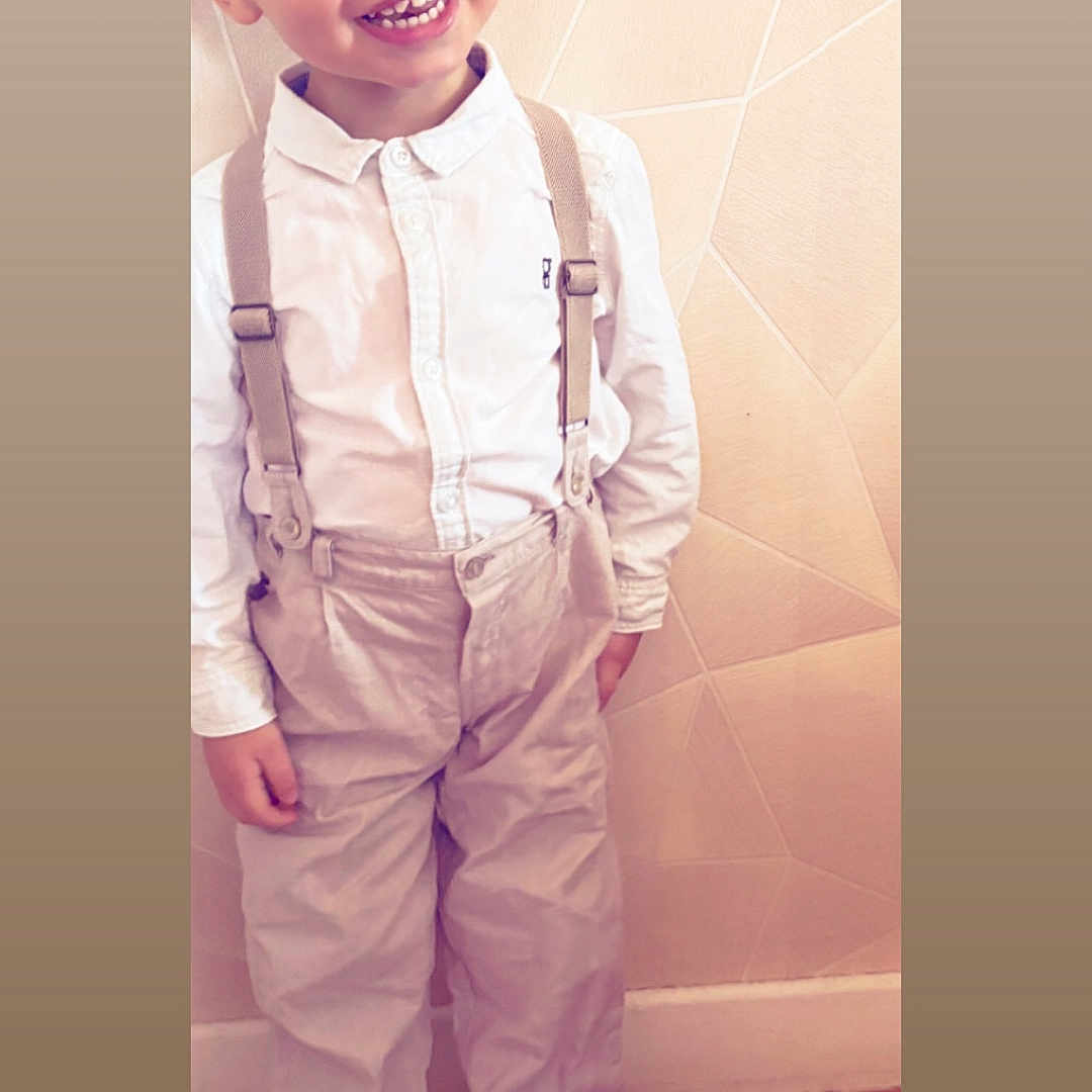 Djulian participe au concours pour gagner de l'argent avec cette photo : child, boy, smiling, standing, suspenders, white_shirt, beige_pants, sneakers, indoor, wall, wooden_floor, happy, cute, portrait, fashion, casual, young, person, clothing, footwear