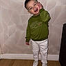 Djulian a rejoint le concours — aidez-le/la à gagner de superbes lots ! child, toddler, smiling, green_sweatshirt, white_pants, white_shoes, indoor, wooden_floor, geometric_wall, standing, playful, cute, casual_clothing, short_hair, person, happy, fashion, casual, portrait, wallpaper