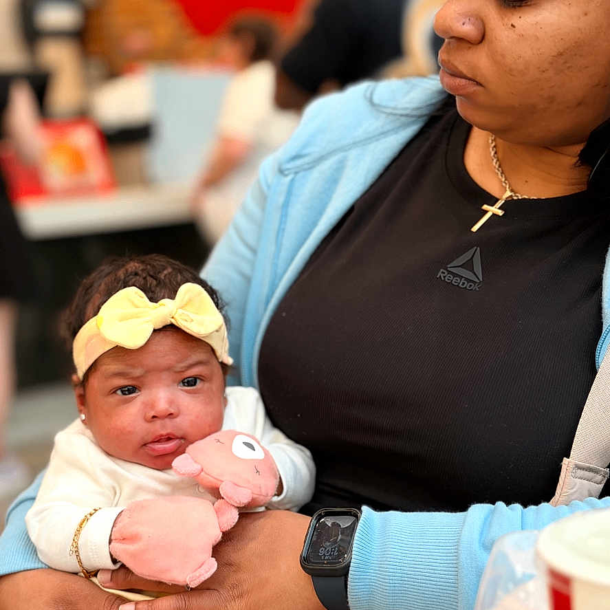 Roxi Love joined the competition — help win amazing prizes! baby, woman, holding, plush_toy, headband, yellow_clothing, black_shirt, watch, cross_necklace, indoor, blurred_background, person, cute, infant, casual, seated, portrait, soft_lighting, modern, technology_overlay