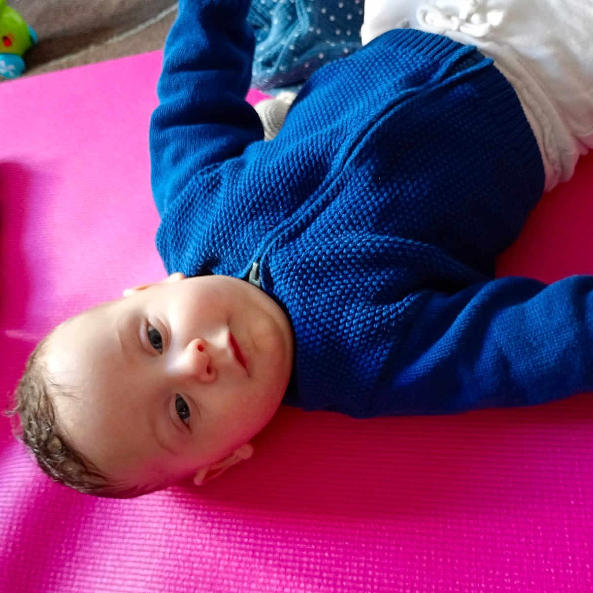 Izaya participe au concours pour gagner de l'argent avec cette photo : baby, blue_sweater, child, closeup, cozy, curious, cute, face, floor, head, indoor, infant, lying_down, person, pink_mat, playing, smile, toy, white_pants, young_child