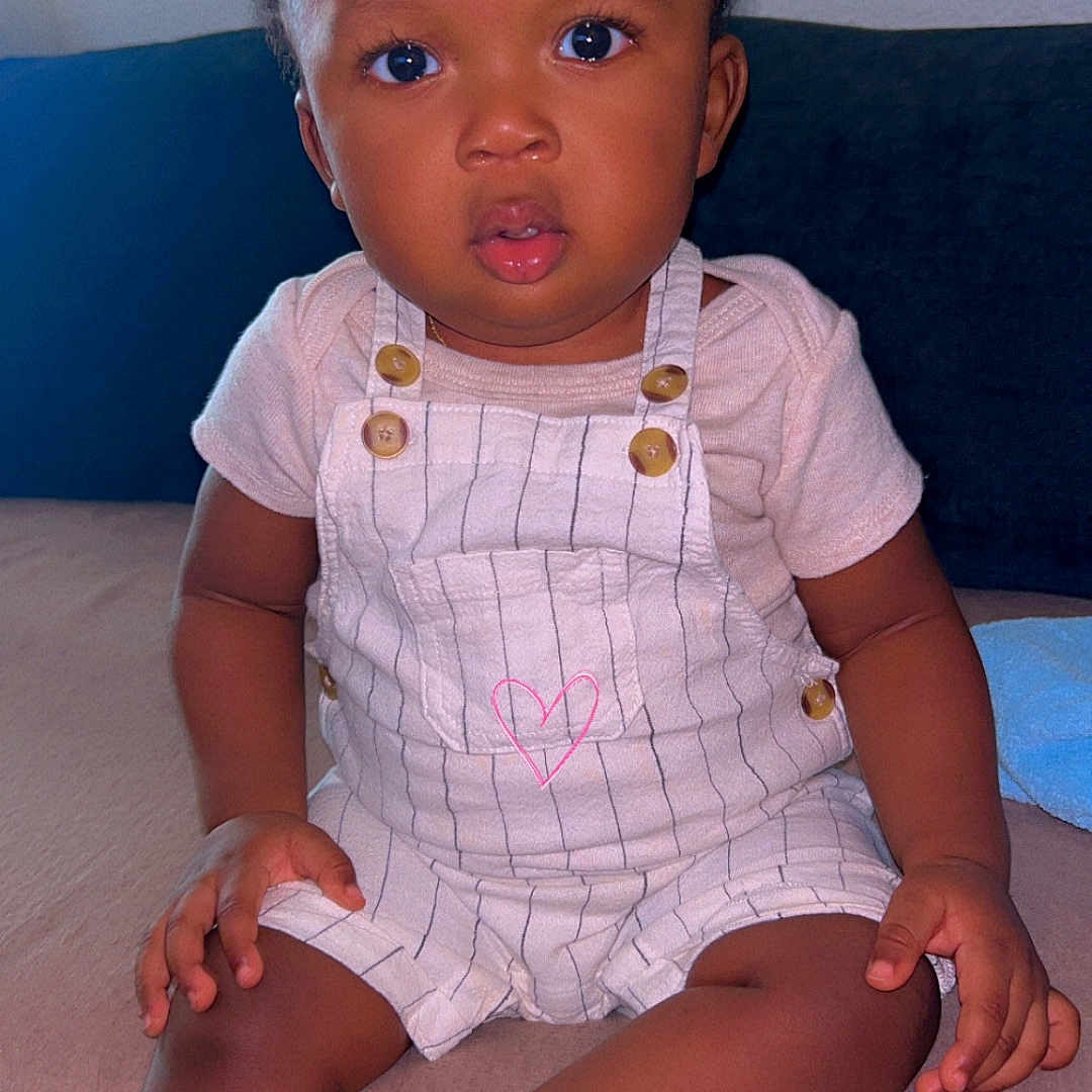 Dwayne participe au concours pour gagner de l'argent avec cette photo : baby, casual, child, clothing, couch, curly_hair, expression, eyes, face, foot, furniture, hand, indoor, overalls, person, pink_heart, sitting, skin, soft, toddler