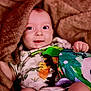 Buck is registered to the contest to win money with this photo: baby, blanket, child, comfort, cozy, cute, dinosaur, face, happy, infant, inside, onesie, person, playful, portrait, smile, soft_toy, toy, warm, young