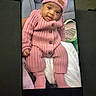 baby, child, infant, portrait, smiling, pink_outfit, knitted_hat, sweater, buttons, socks, seated, tablet, screen, electronic_device, indoor, blanket, cushion, closeup, photograph, fashion