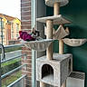 cat, cat_tree, plush, toy, knitted_fish, window, brick_wall, residential_building, balcony, daylight, indoor, pet, relaxed, feline, hammock, scratching_post, cozy, home, green_wall, heater