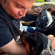 Drogon joined the competition — help win amazing prizes! man, dog, rottweiler, car, steering_wheel, tattoo, arm, black_shirt, sunlight, window, closeup, pet, companion, affection, interaction, portrait, indoor, animal, human, friendship