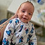 baby, infant, smile, onesie, clothing, person, arm, tattoo, face, happy, indoor, holding, cute, child, apparel, pattern, portrait, baby_clothes, closeup, soft_focus